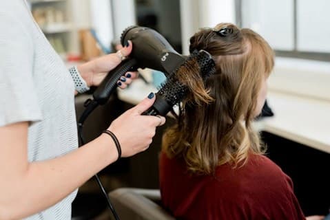 Una estilista seca el pelo de una clienta en una peluquería.